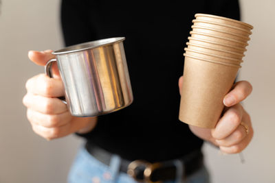 Woman in black shirt holding paper cup and metal reusable mug. sustainable choice. ecology lifestyle