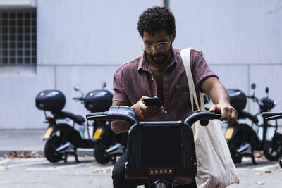 Contemplating man using mobile phone on rented bicycle in city