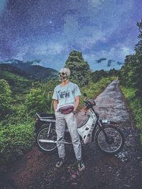 Man with bicycle standing on mountain against sky