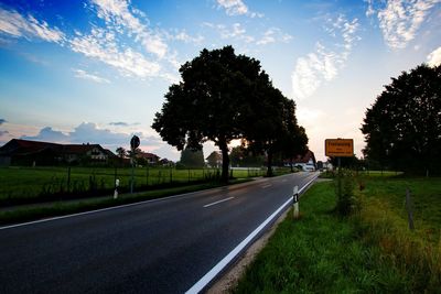 Empty road on grassy field against sky during sunset