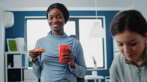 Portrait of young woman using mobile phone while standing in office