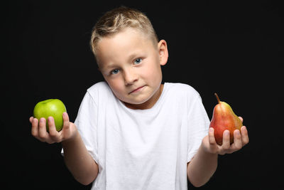 Portrait of boy holding apple against black background