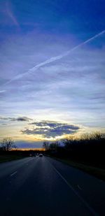 Road by trees against sky during sunset