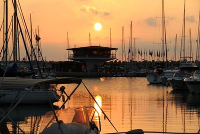 Sailboats moored at harbor against sky during sunset