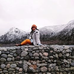 Man sitting on rock by mountain against sky