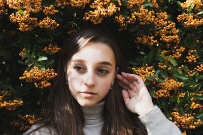 Close-up of thoughtful young woman standing against orange berries on plant