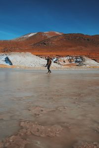 Man walking on salt lake against mountains during sunny day