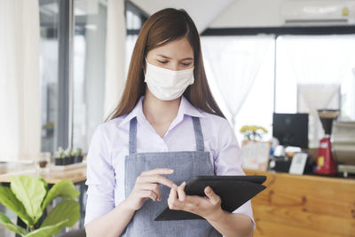 Young woman using digital tablet while wearing mask