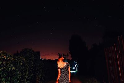 Rear view of woman standing against sky at night