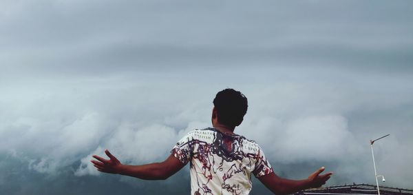Rear view of man with arms raised against sky