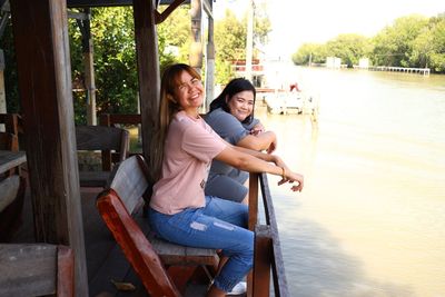 Happy friends sitting on bench by railing