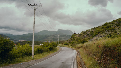 Road by electricity pylons against sky
