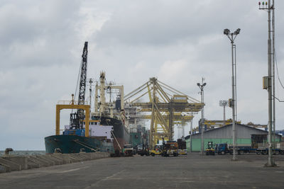 Cranes at harbor against cloudy sky