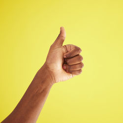 Cropped hand gesturing against yellow background