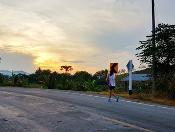 Rear view of woman on road against sky during sunset