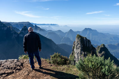 Rear view of man standing on mountain against sky