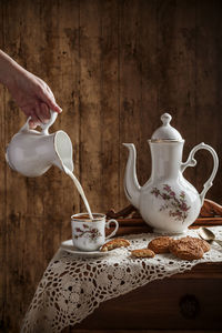 Hand pouring milk into coffee served on vintage tableware with cookies