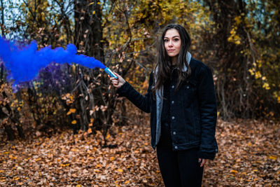 Young woman holding distress flare while standing in forest during autumn