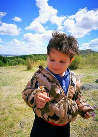 Boy holding flower while standing on grassy field