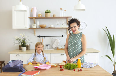 Portrait of smiling mother preparing food at kitchen with daughter