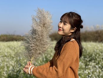 Side view of young woman standing on field against sky