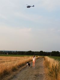 Full length of girl standing with dog on dirt road during sunset