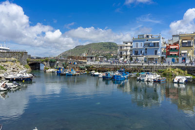 Sailboats moored on river by buildings against sky