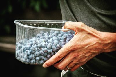 Cropped image of person carrying blueberries in plastic container