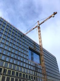 Low angle view of crane by building against sky