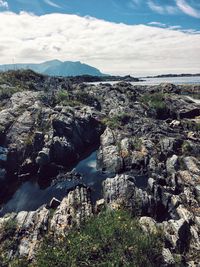 Scenic view of sea and rocky mountains against cloudy sky during sunny day