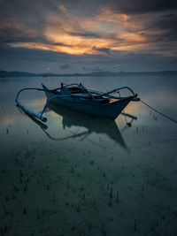 Boat moored in sea against sky during sunset