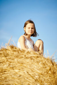 Cute little girl sits on mown rye in the field in summer