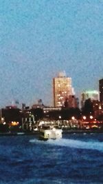 Illuminated city by sea against sky at dusk