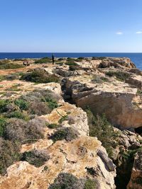 Rocks by sea against clear blue sky