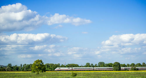 Train moving by grassy landscape against sky