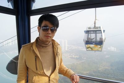 Portrait of man wearing sunglasses standing by window of overhead cable car