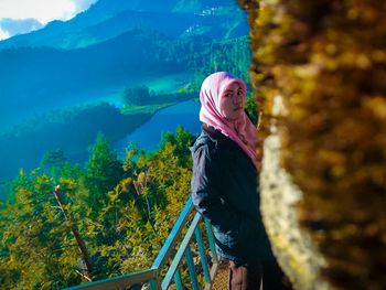 Side view of woman standing by railing against trees