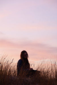 Woman sitting on field against sky during sunset