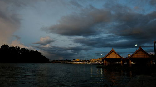 Houses by lake and buildings against sky at dusk