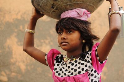 Close-up of girl carrying container on head against wall