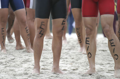 Low section of people standing on sand at beach