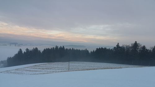 Snow covered field against sky during sunset