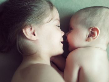 Directly above shot of shirtless siblings lying face to face on bed