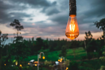 Close-up of illuminated light bulb against sky during sunset