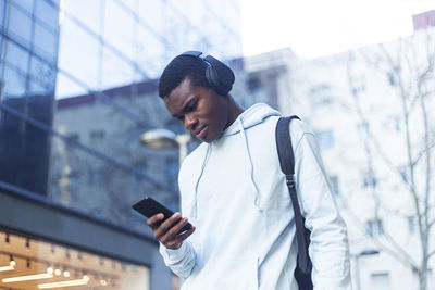 Young man listening to music while using phone outside building