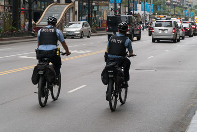 Rear view of people riding bicycle on city street