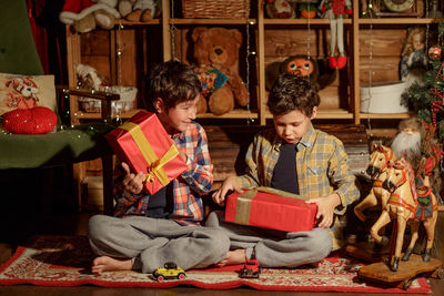 Two real brothers lie in a room with new year's decor near an armchair and look at gifts