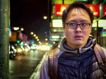 Portrait of young man in illuminated city street scene at night.