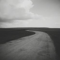 Road passing through field against cloudy sky