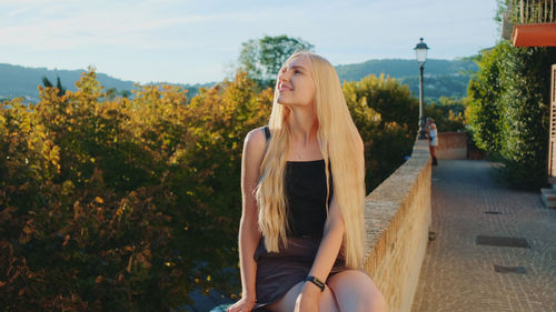 Young woman sitting on plant against trees